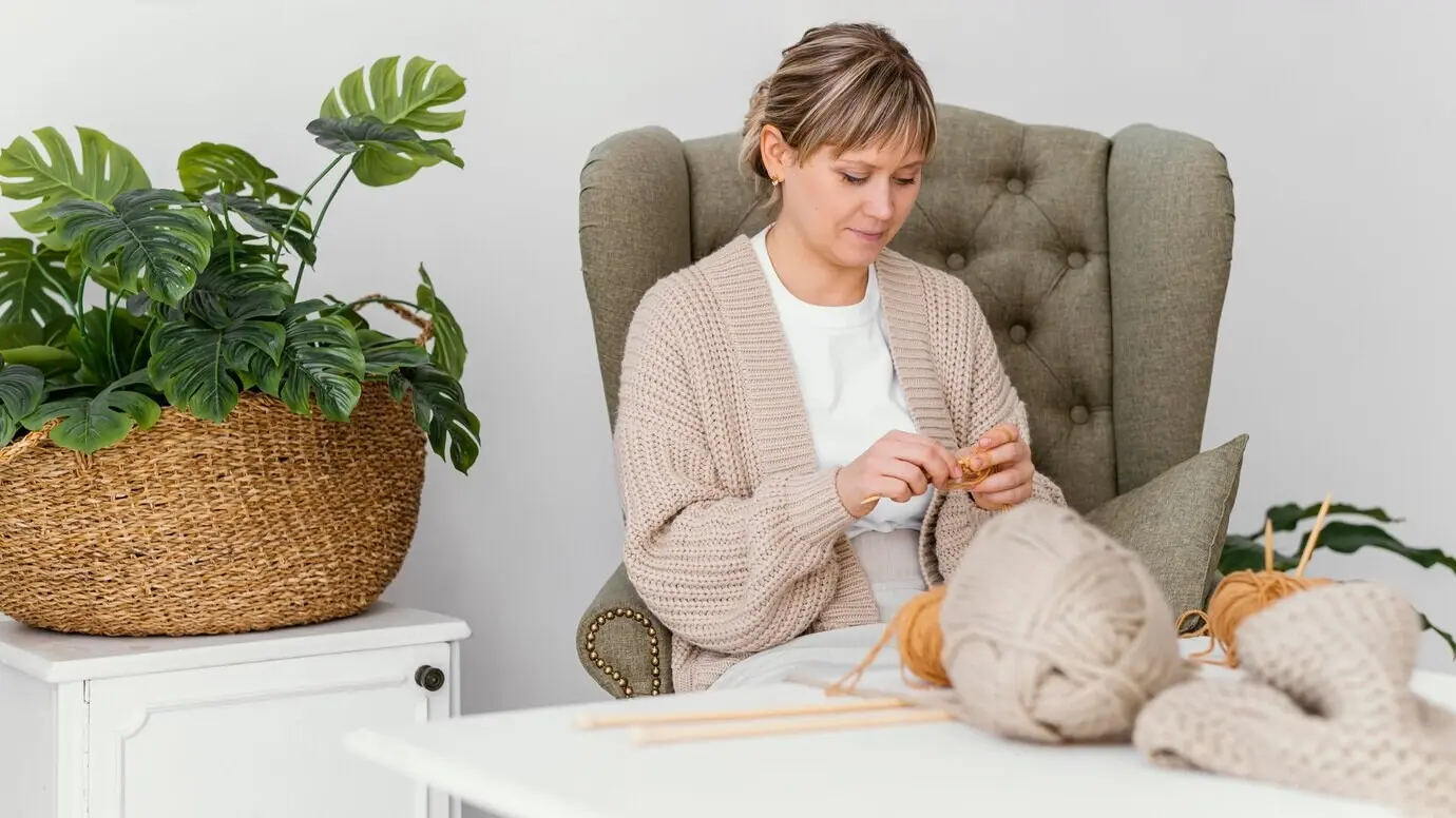 Halbnahe Aufnahme einer strickenden Frau zu Hause.