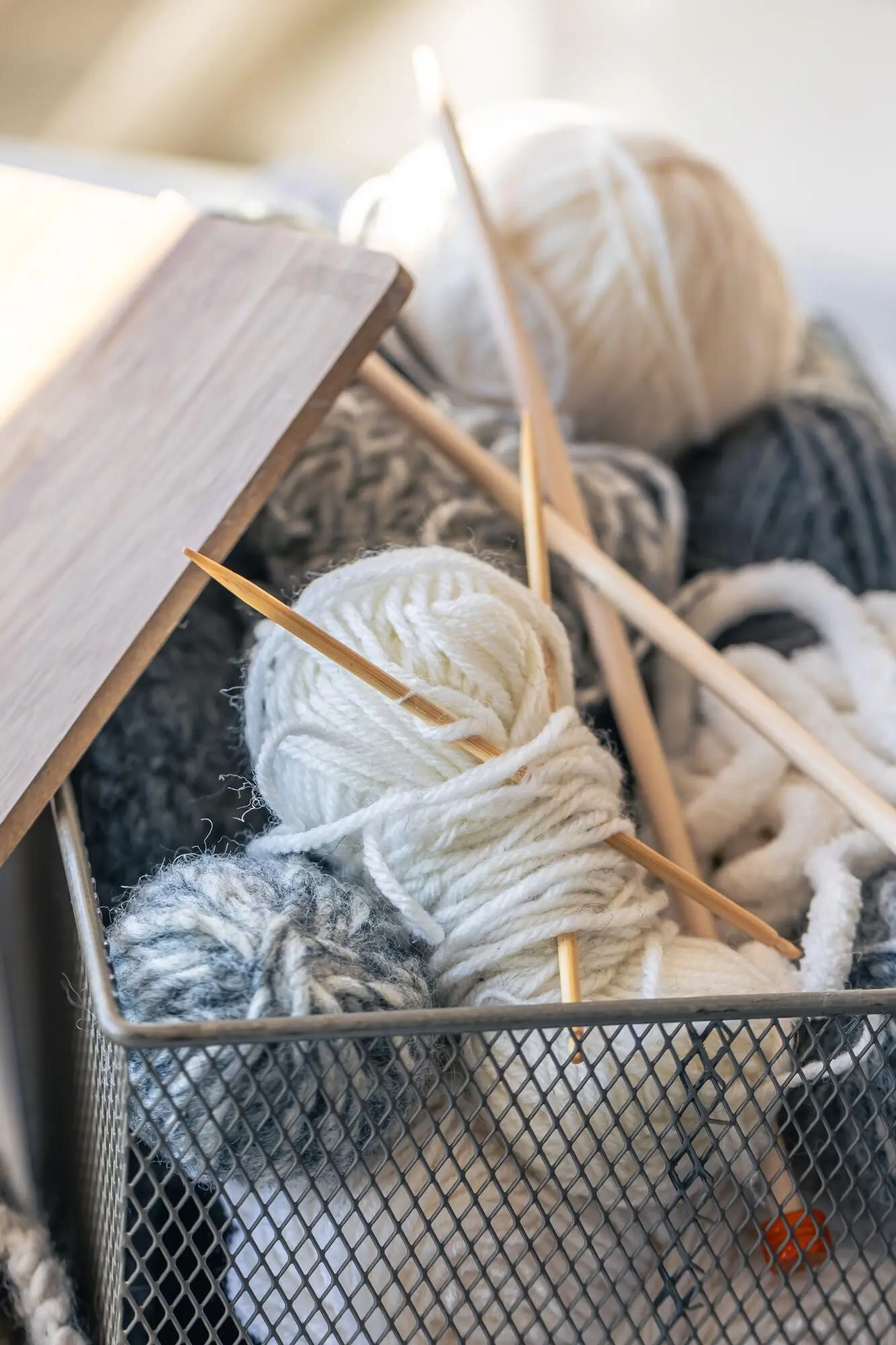 Schachtel mit Garnfäden und hölzernen Stricknadeln.