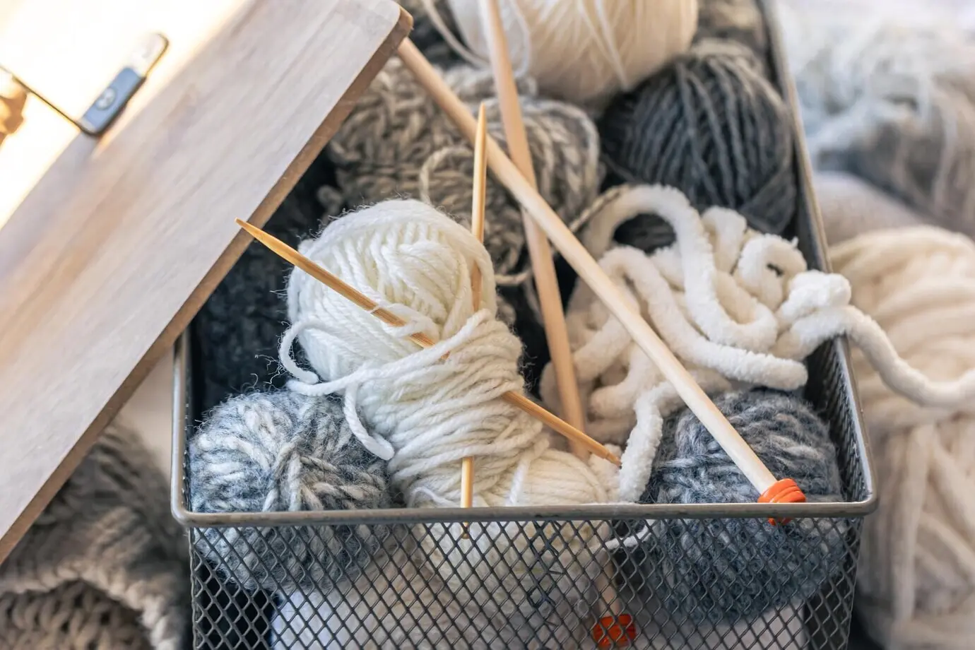 Schachtel mit Garnfäden und hölzernen Stricknadeln